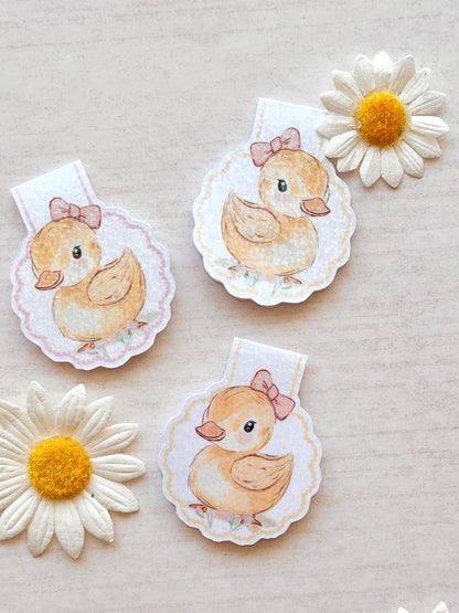 Three duckling magnetic bookmarks with flowers on a beige background