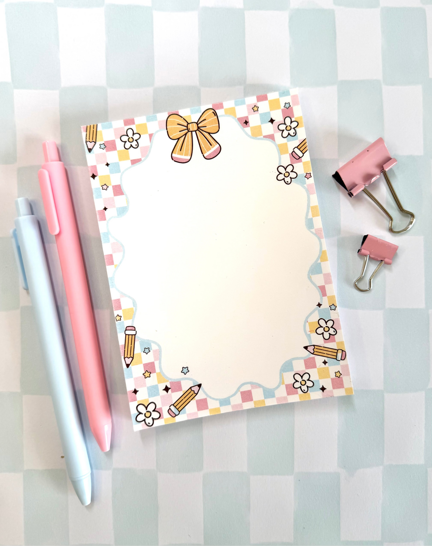 Notepad with decorative border, pens, and clips on a checkered background